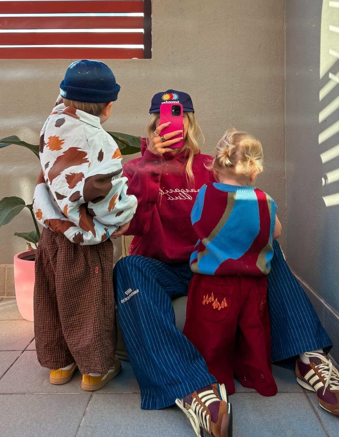 Ash Sambell and kids in colorful outfits taking a selfie outdoors wearing cow print jacket