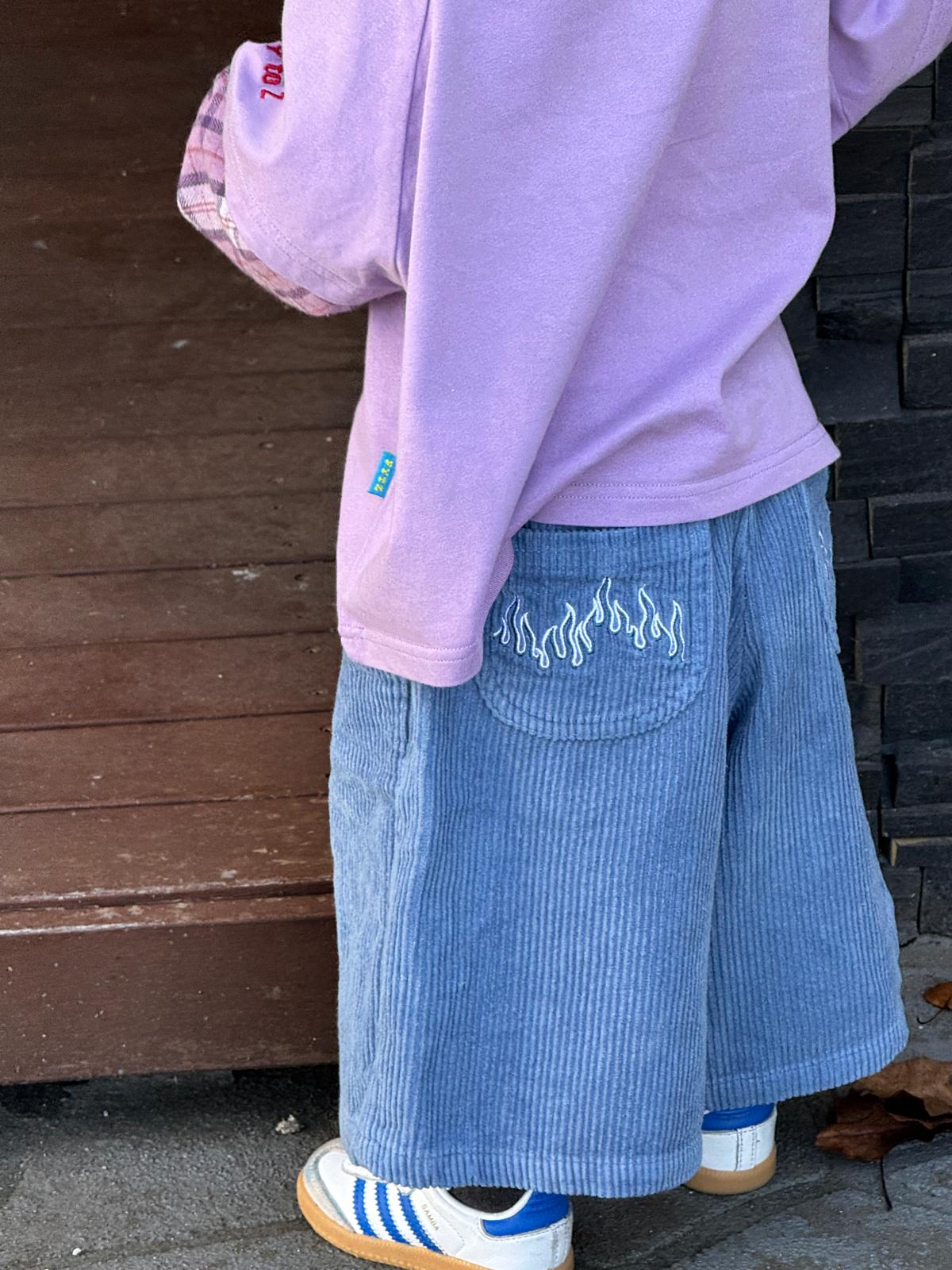 Person wearing a light purple hoodie and blue corduroy pants with flame design.