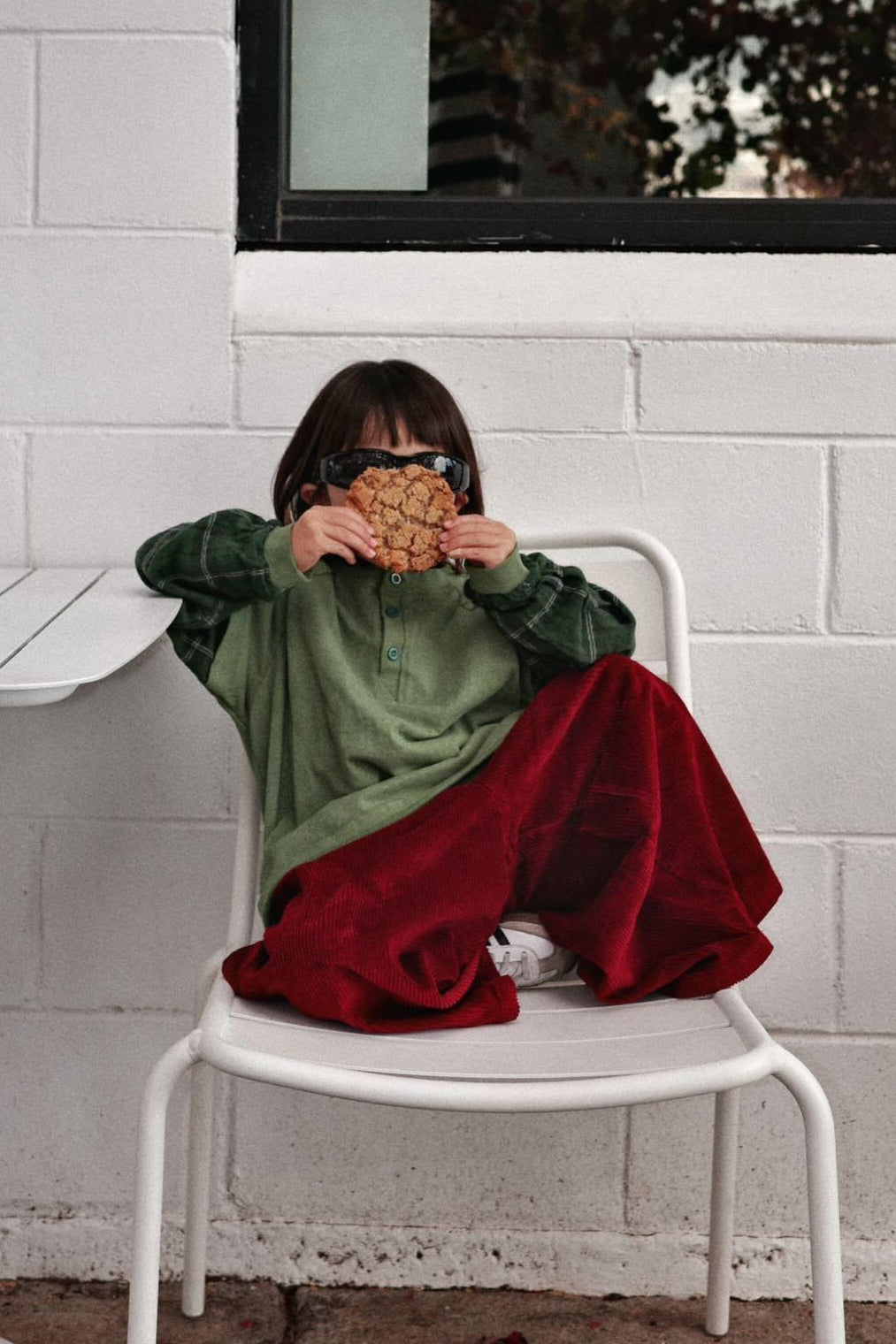 Child sitting on a chair holding a cookie wearing blaze corduroy pants and ollie doublesleeve plaid tee in hunter green
